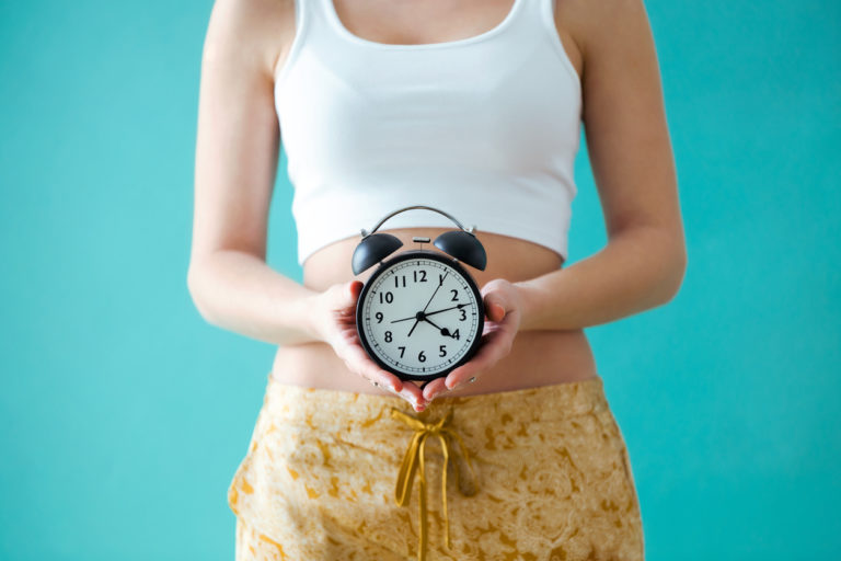 young woman holding a clock in front of her body while waiting for Beverly Hills plastic surgery