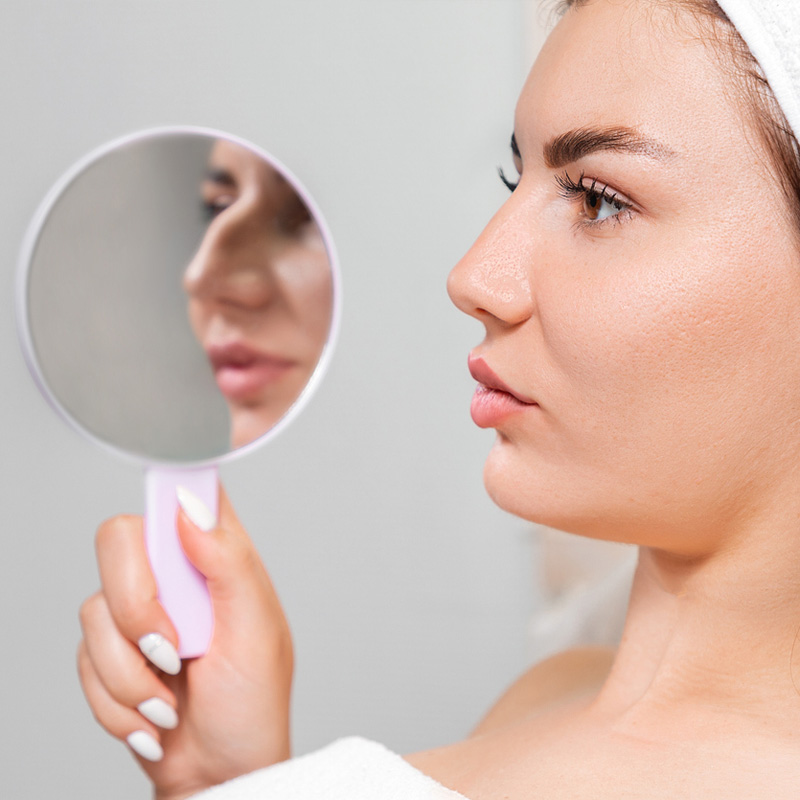 stock image of model seeing her face in mirror holds with one hand