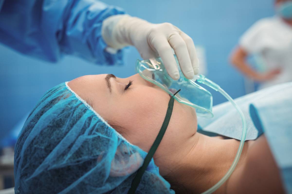 A woman in a hospital gown is receiving oxygen through a mask, indicating medical care and support.