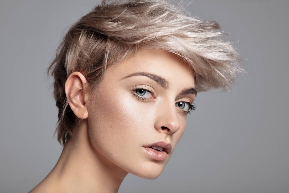 A woman with short blonde hair, smiling softly, stands against a neutral background, exuding confidence and warmth.