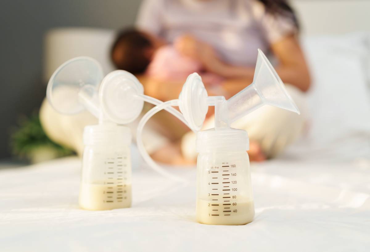 Closeup of milk in bottle, woman breastfeeding in the background.