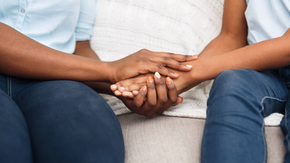 Two individuals seated on a couch, holding hands, symbolizing connection and companionship.