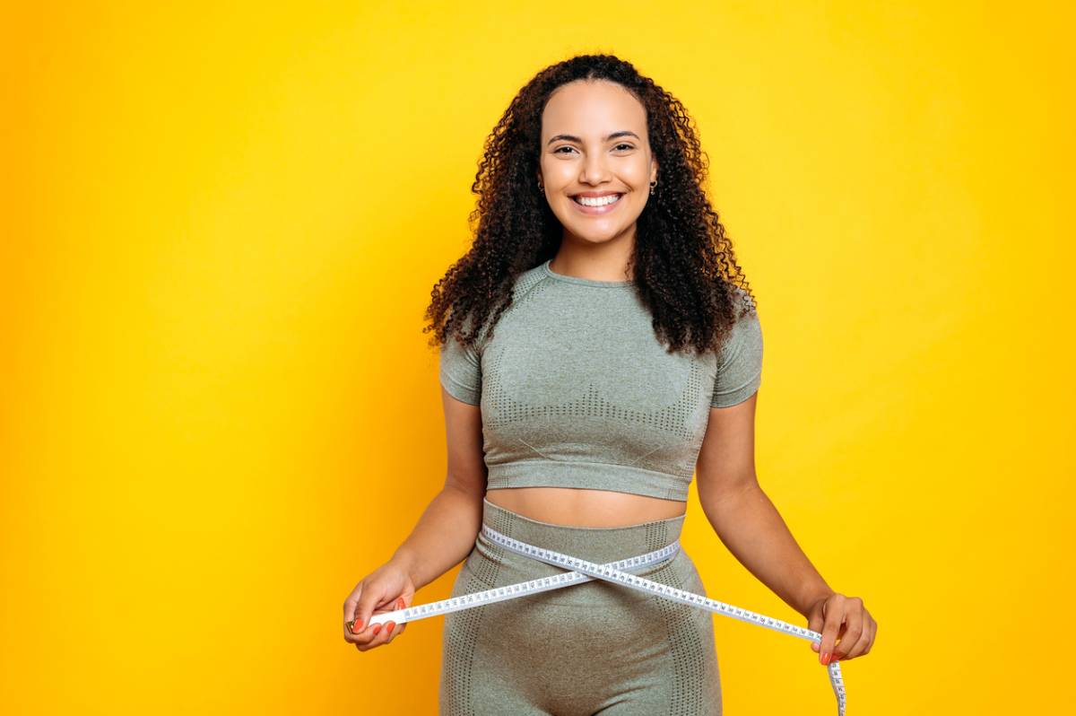 A woman in a grey top and shorts holds a measuring tape, preparing to take measurements for a project or task.