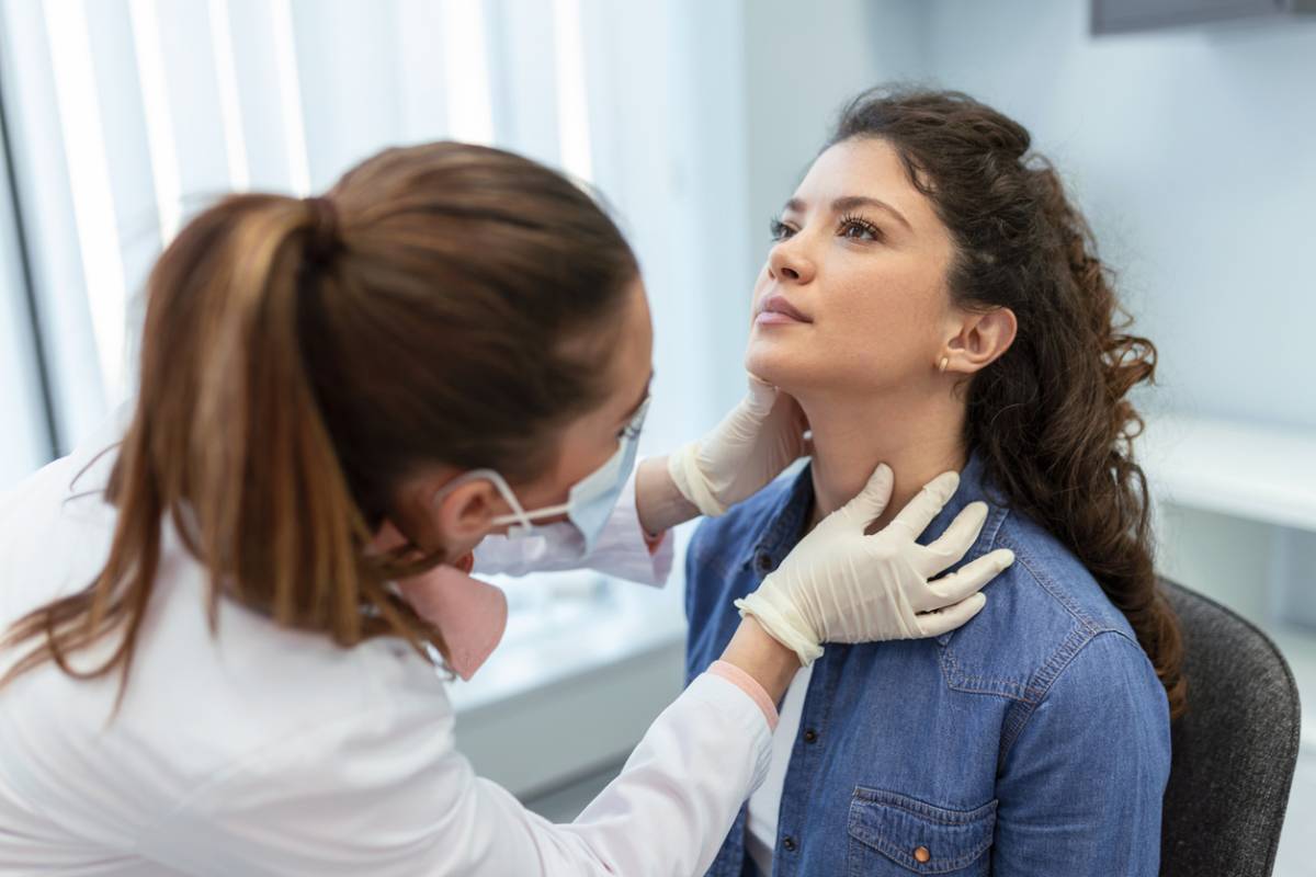 A doctor examines a woman's neck during a medical check-up in a clinical setting.