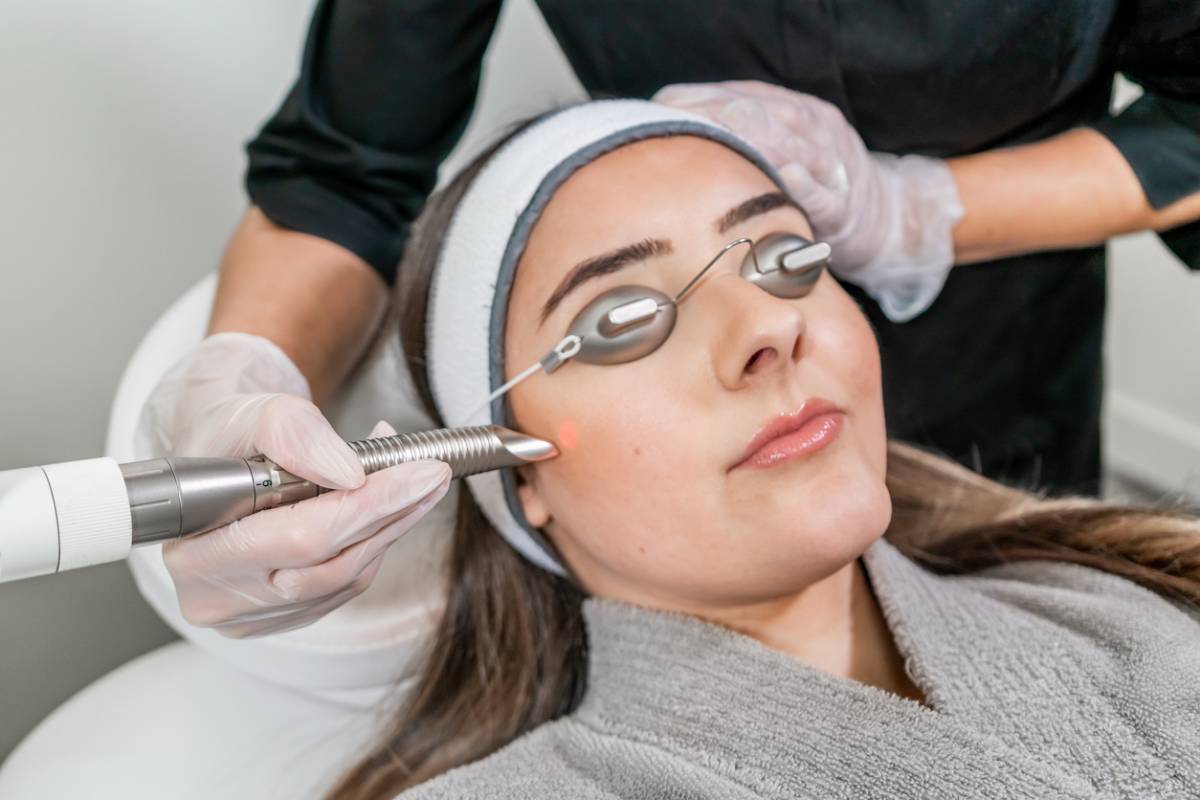 A woman undergoing a laser treatment, focused and relaxed in a clinical setting, with equipment visible in the background.