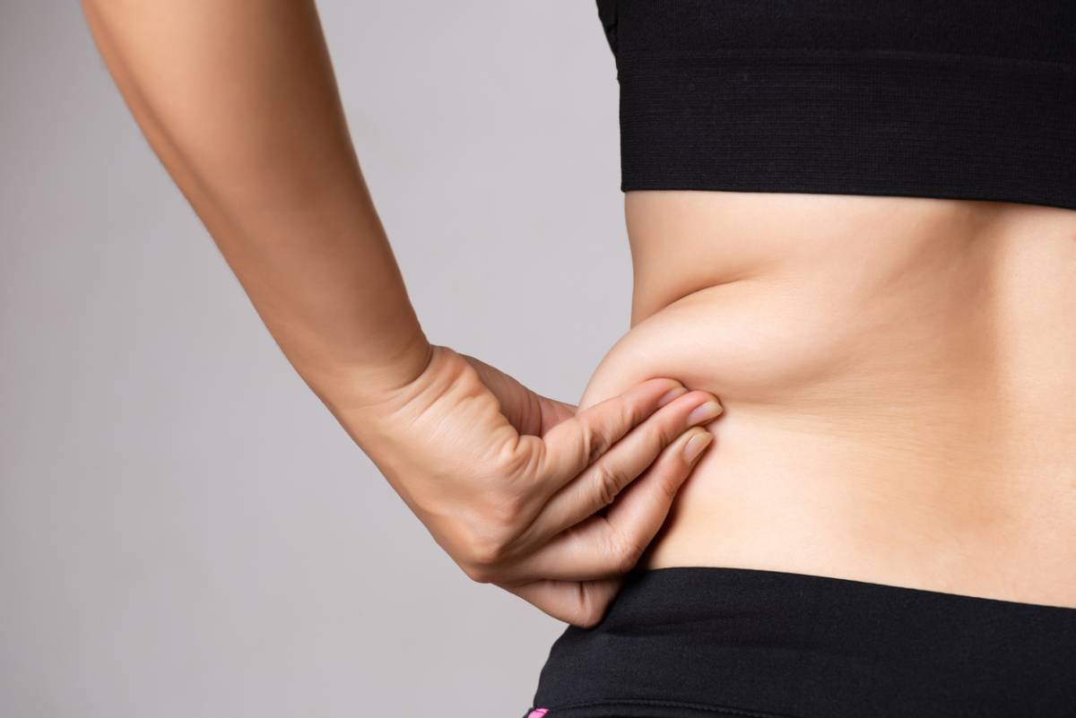 A woman stands confidently, showcasing her belly, with a warm smile and a relaxed posture.